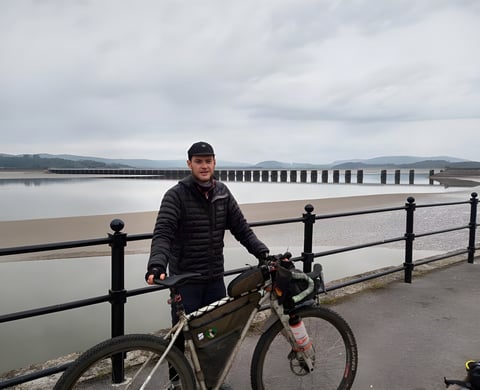 Rider with a mud-spattered bikepacking bike on the seafront at Arnside, where the Dales Divide 2021 starts.