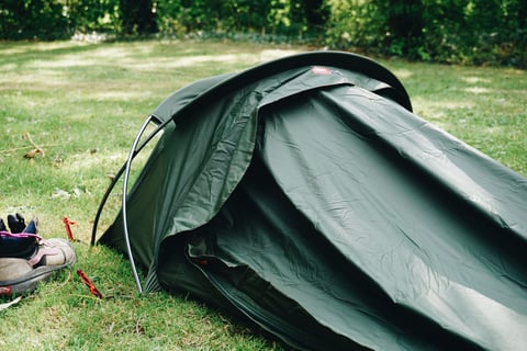Green Alpkit Elan hooped bivvy pitched on grass, its head-end hoops holding up the hood, with a pair of boots beside it.
