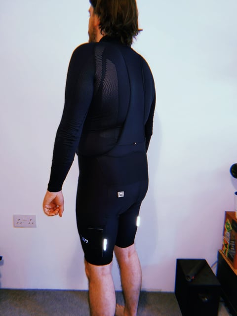 Rear view of the Santini Gravel Bib shorts over a long-sleeved base layer, showing reflective tabs and a mesh thigh pocket.