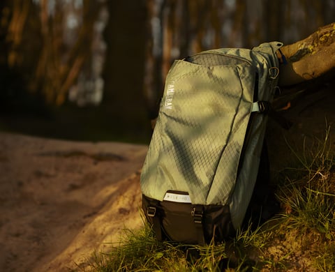 A khaki Camelbak Mule Pro hydration pack rests against a tree on a woodland path.