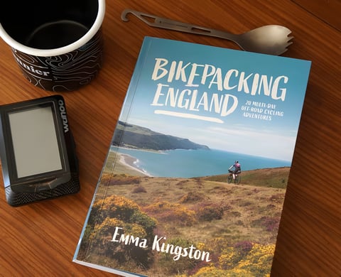 Cover of Bikepacking England by Emma Kingston, beside a Wahoo bike computer, mug and spork.