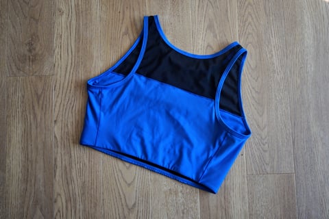 Back of the blue Foundations Sports Bra with mesh upper back panel, laid on a wooden floor.