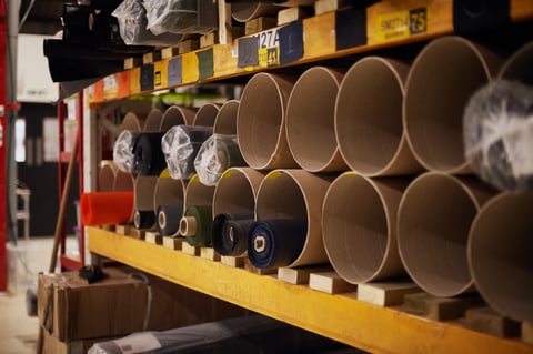 Rolls of fabric in cardboard tubes stacked on racking in the Restrap workshop, raw material for the bags.