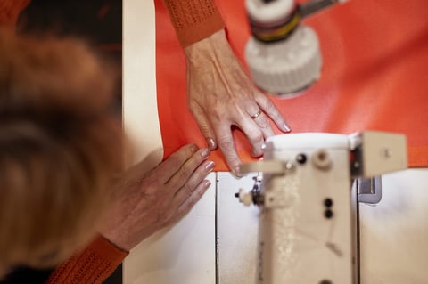 Overhead view of hands feeding orange fabric and a cream strap under a sewing machine foot at Restrap.