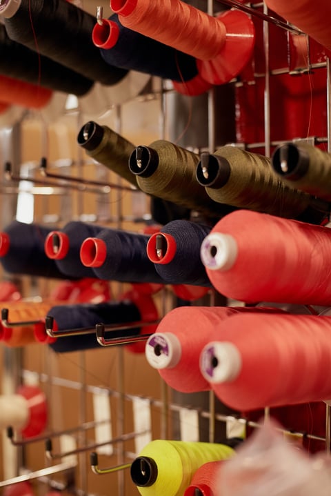 Cones of red, navy, olive and yellow sewing thread on a wire rack in the Restrap workshop.