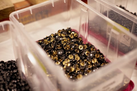 Plastic tub of black and brass poppers waiting to be fitted to Restrap bags.