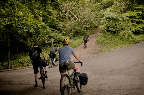 Riders on gravel bikes leave a country lane for a dirt bridleway climbing into woodland near Leeds.