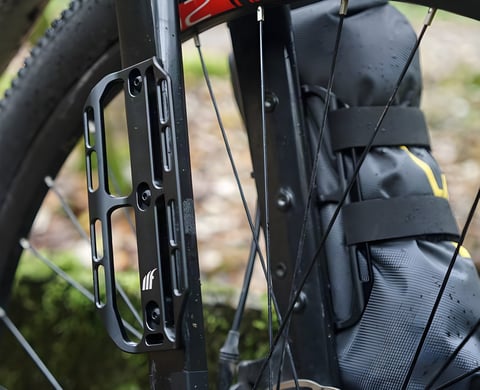 Close-up of a black Tailfin Cargo Cage bolted to a fork leg, next to a strapped-on Apidura fork pack.