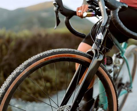 Close-up of a WTB Carbon CZR front wheel with a tan-wall Resolute tyre on a teal gravel bike on a hillside track.