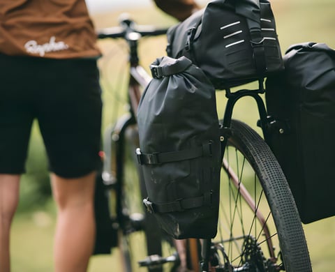 Pair of black Tailfin Mini Panniers clamped to a rear rack with a bag on top, a rider standing beside the bike.