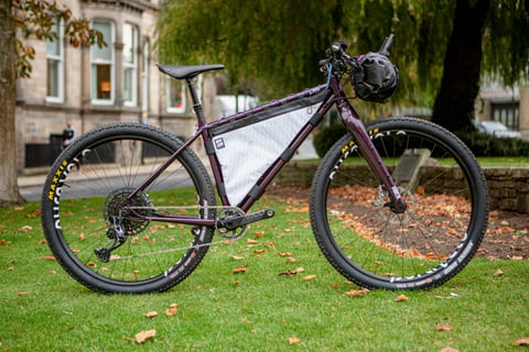 Lord Cycles Nomad rigid mountain bike in purple with frame bag and handlebar bag, parked on grass at Bespoked.