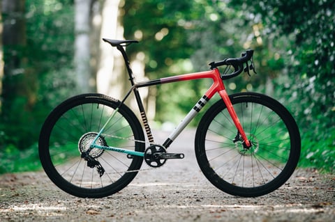 2021 Specialized Crux gravel bike in red, white and teal, side view on a gravel track through woodland.