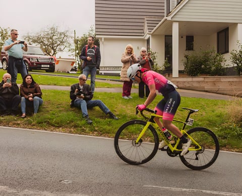 Women's Tour of Britain rider in pink on a yellow Cannondale climbs Hambro Hill past roadside spectators.