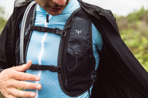 Rider in a light blue jersey and open black jacket wears the Apidura Racing Hydration Vest, chest straps clipped.