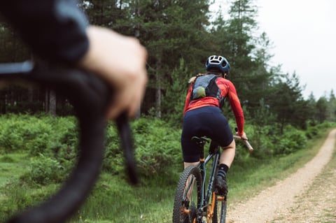 Rider wearing the Apidura Racing Hydration Vest heads away down a gravel track between pine trees.