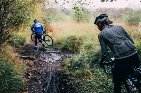 Rider follows another through a muddy, rutted woodland trail on the Peak District Gravel Bonanza route.