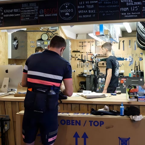 Chris Hinds at the counter of The Woods Cyclery bike shop during the Great British Divide, with the workshop behind.
