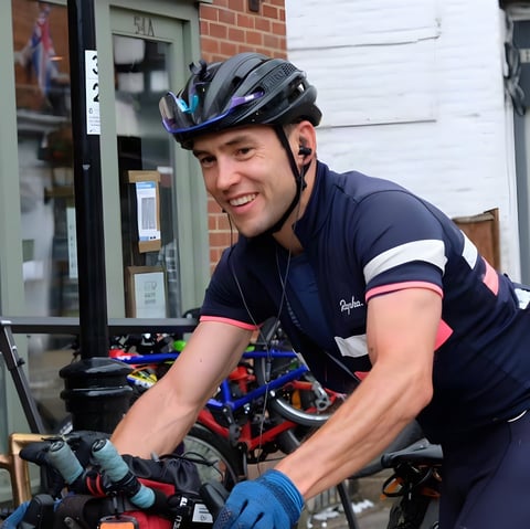 Chris Hinds smiles in a helmet and Rapha kit beside a rack of bikes during the Great British Divide.