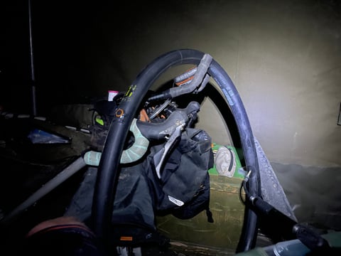 Spare inner tube hung over a bike's handlebars and bag inside a dark tent, lit by torchlight after a night puncture.