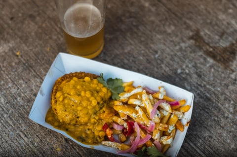 Pie under yellow curry sauce with loaded chips and pickled onion in a tray, and a pint of beer, at the Gravel Bonanza finish.
