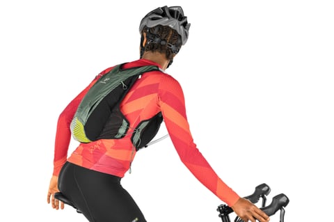 Rear view of a rider on drop bars in a studio, showing the green back panel and low fit of the Apidura Racing Hydration Vest.