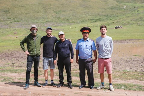 Five people pose on a muddy hillside in Kyrgyzstan, one in a uniform and peaked cap, during the Silk Road Mountain Race.