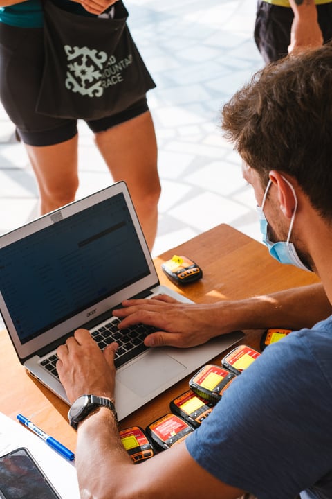 Silk Road Mountain Race staff member works at a laptop beside a row of GPS trackers on a desk.