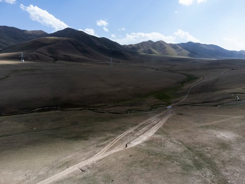 Aerial view of a rider on a dirt track crossing open hills in Kyrgyzstan during the Silk Road Mountain Race.