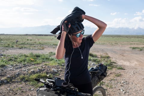 Silk Road Mountain Race rider pulls a jumper off over a helmet beside a loaded bikepacking bike in Kyrgyzstan.