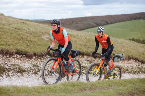 Two riders with bikepacking bags climb a steep chalk track on loaded gravel bikes on the Isle of Wight.