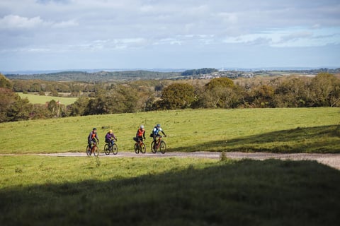Four riders on a gravel track crossing green farmland, with woodland and distant views across the Isle of Wight.