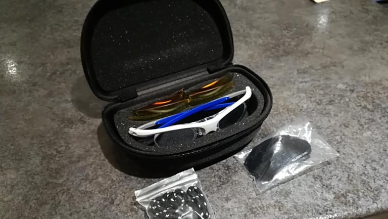 Optilabs Swift glasses in their black foam-lined case, with spare shields in plastic bags beside it.
