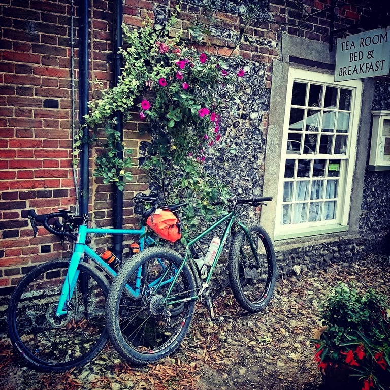Green Surly Krampus and blue Pinnacle Arkose lean against the flint wall of a tea room in Castle Acre, Norfolk.