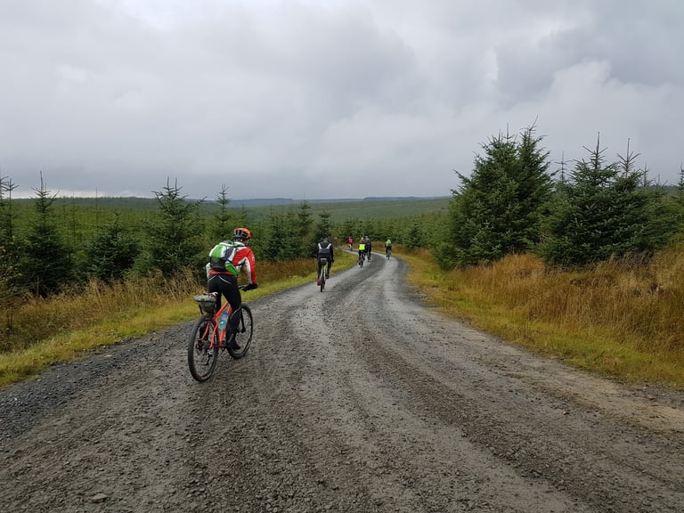 Gravel Rocks Training Camp group heading out on a wide gravel road through Kielder Forest on a grey day.