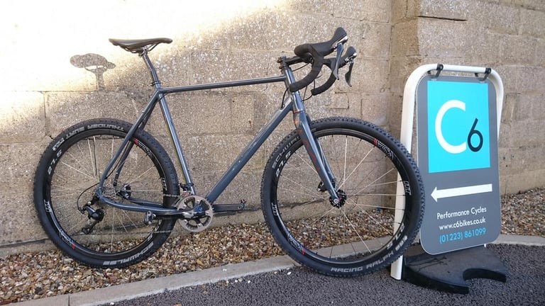 Grey Mason Bokeh built with 650b wheels and knobbly tyres, parked beside a bike shop sign.
