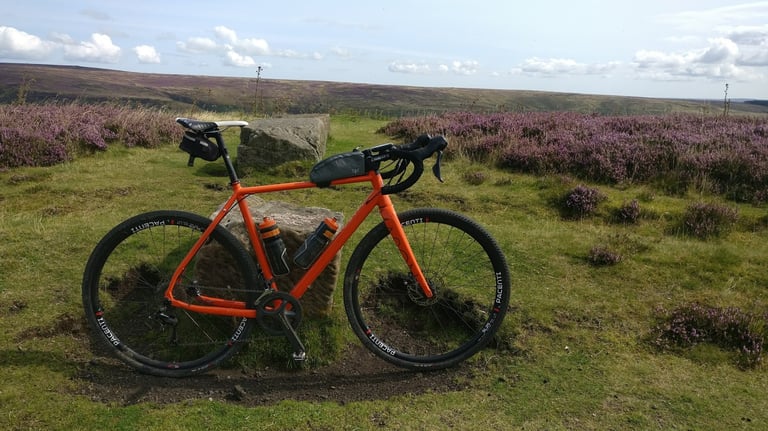 Orange Mason Bokeh with top tube bag and saddle bag leaning on a boulder among heather on the North York Moors.