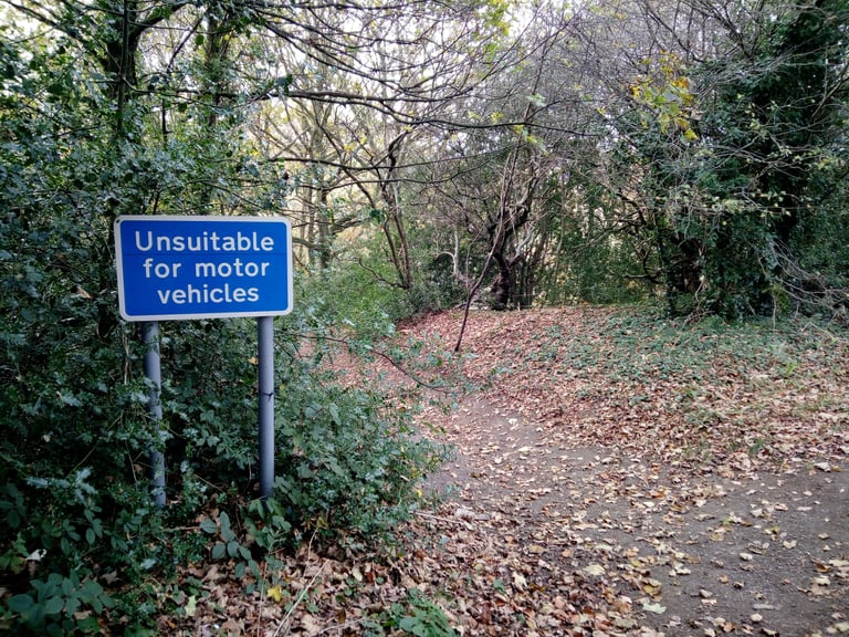 Blue 'Unsuitable for motor vehicles' sign at the start of a leaf-strewn bridleway on the Hardcore 100 route.