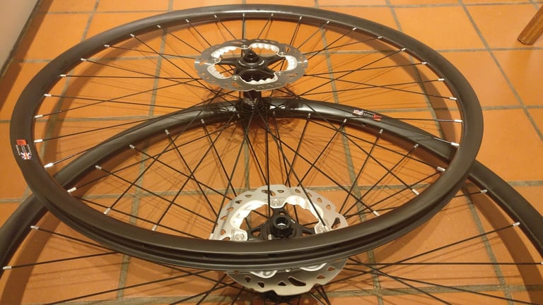 Freshly built carbon gravel wheels on Hope RS4 hubs with disc rotors fitted, no tyres yet, lying on a tiled floor.