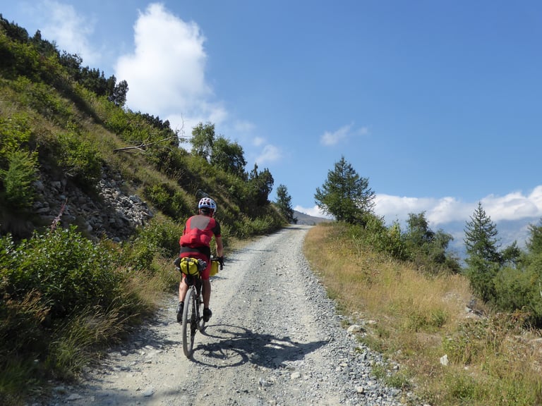 Rider with a bar bag climbs a gravel mountain road in the sun, the marketing dream of adventure cycling.