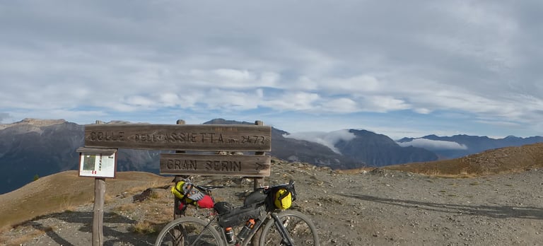 Loaded Pinnacle Arkose beside the Colle dell'Assietta sign at 2,472m, with mountains and cloud behind.