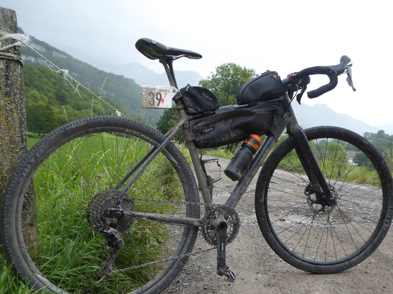 Mud-splattered Pinnacle Arkose loaded with Wildcat bags and a race number, parked on a gravel track below hills.