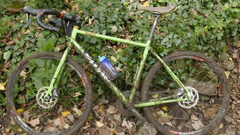 Muddy green Cotic drop-bar bike lying in ivy and fallen leaves, the kind of bike suited to the Hardcore 100.