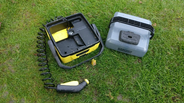 Kärcher OC3 portable washer with its coiled hose unreeled from the open base and spray gun laid on the grass.