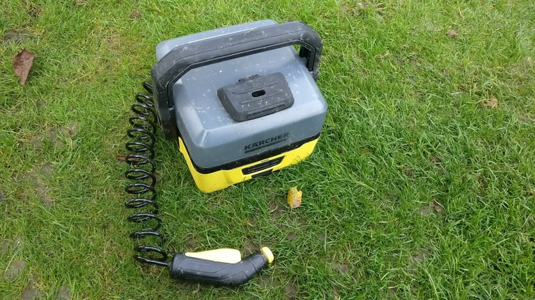 Kärcher OC3 portable bike washer reassembled on grass, with its coiled hose and spray gun ready to use.