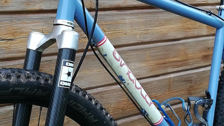 Close-up of the Singular Swift's On One carbon fork and downtube, with scuffed paint and a mud-caked tyre.