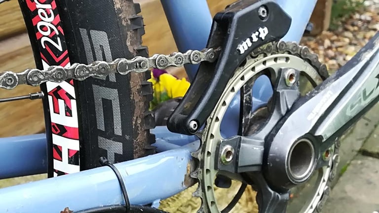 Singular Swift drivetrain with Shimano SLX crank, single chainring and MRP chain guide beside a muddy tyre.