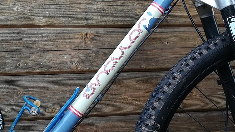 Flaking decal and chipped blue paint on the downtube of the Singular Swift, next to a muddy front tyre.