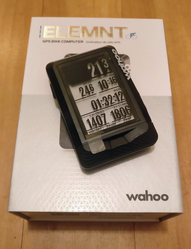 Wahoo ELEMNT bike computer, front view, resting on its retail box on a wooden table.