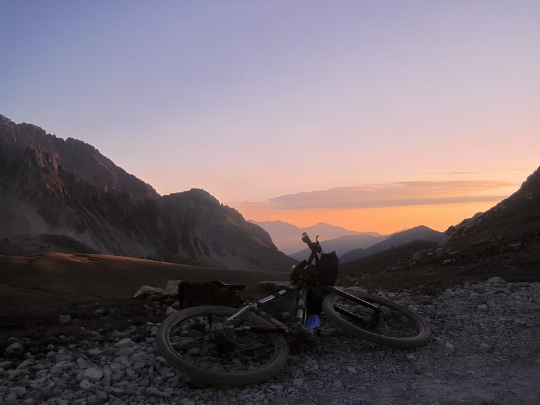 Loaded bike lying on stony ground at sunset above Maritime Alps valleys on the Torino-Nice Rally.