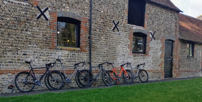 Row of Mason demo bikes propped against the flint and brick wall of the barn, with a lawn in front.